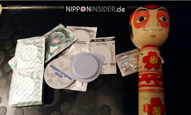 Kondomverpackungen von japanischen und deutschen Kondomen liegen zusammen mit einer Kokeshi auf dem Tisch | Nipponinsider